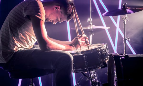 pensive man playing the drums, playing the drums with sticks close-up. Against the background of colored lights and a bright beam of light. Musical concept with a working drum.