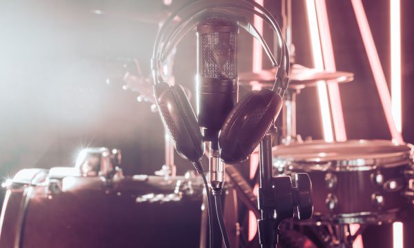 Studio microphone and headphones on a close-up stand, in a recording Studio or concert hall, with a drum set in the background in out-of-focus mode. Beautiful blurred background of colored lights.