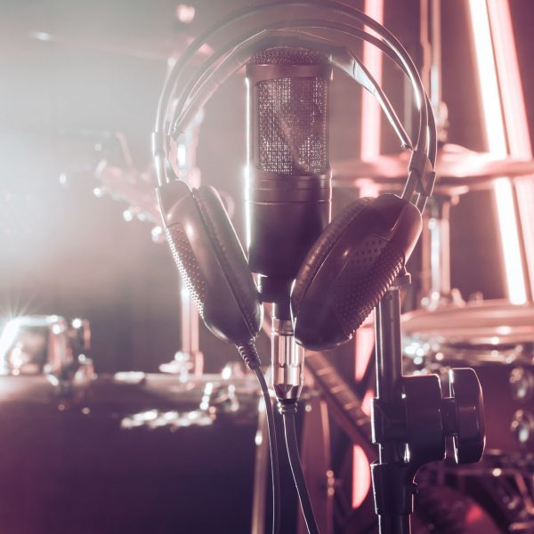 Studio microphone and headphones on a close-up stand, in a recording Studio or concert hall, with a drum set in the background in out-of-focus mode. Beautiful blurred background of colored lights.